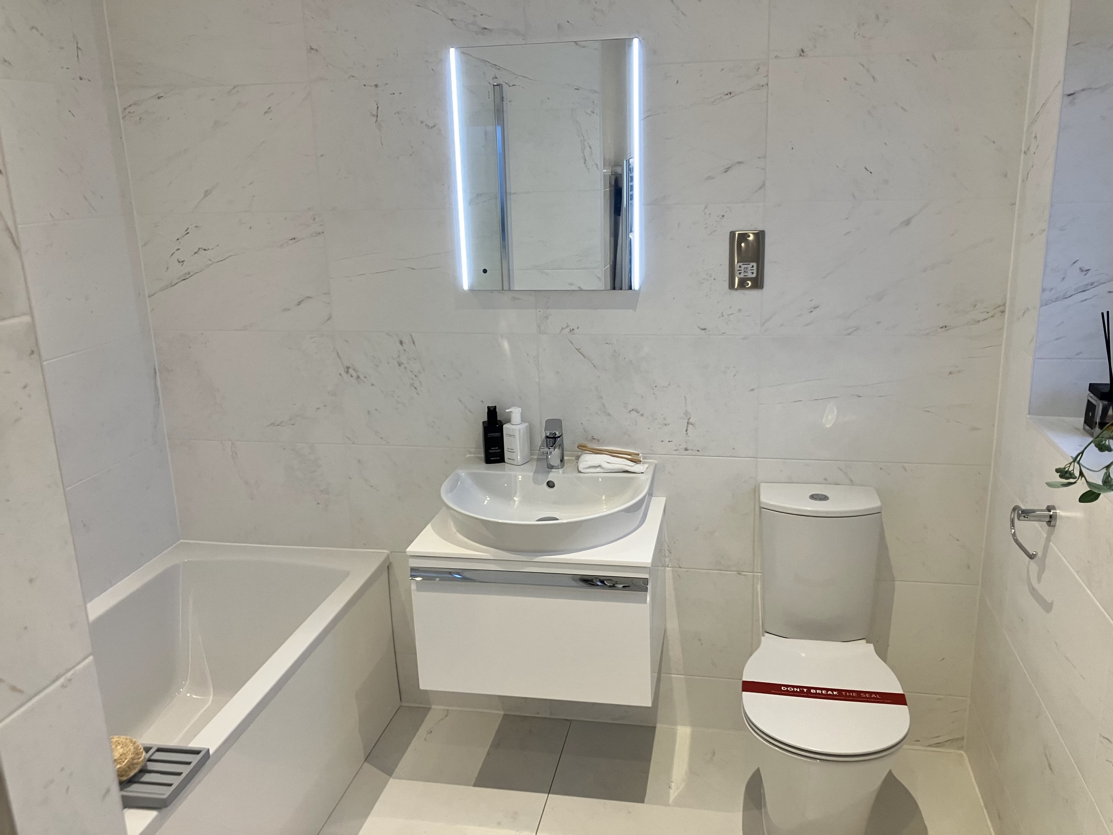 Bright white marble-tiled bathroom with bathtub and wall-hung vanity sink