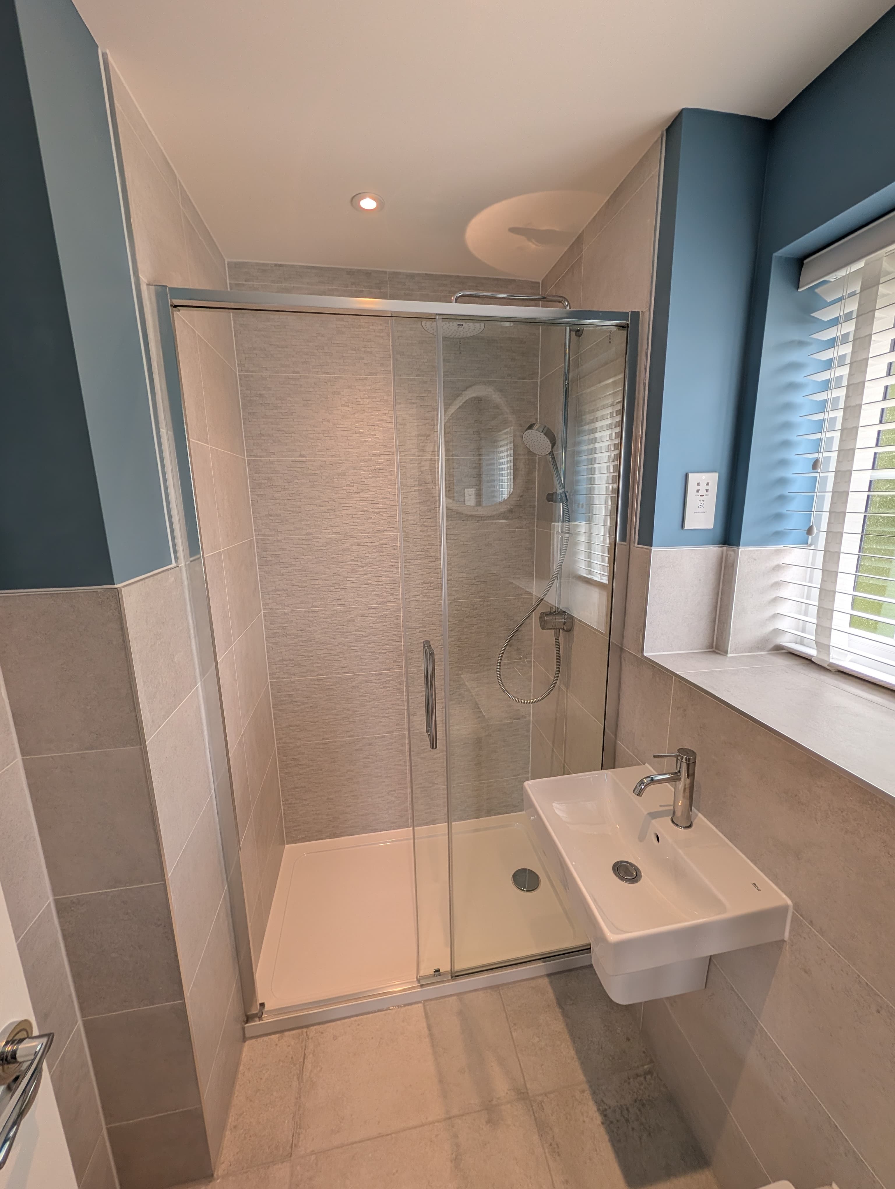 Glass shower enclosure with circular mirror against a blue accent wall