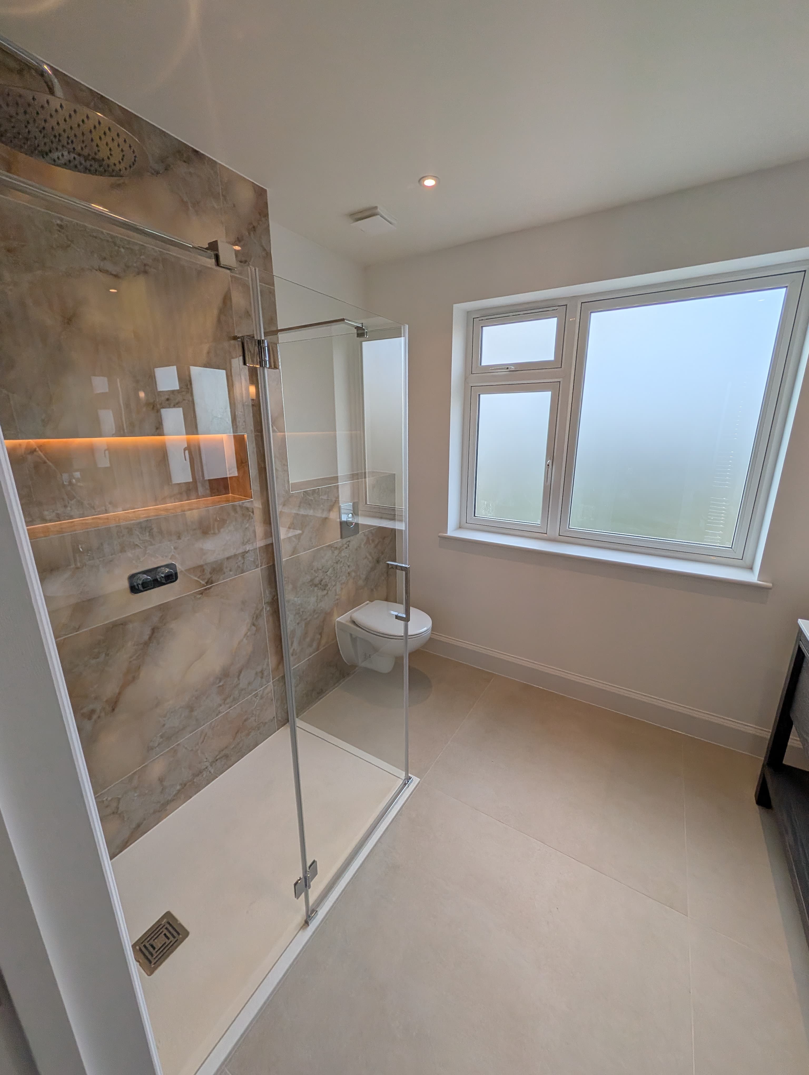 Book-matched marble-effect shower wall with a backlit recessed niche, chrome fittings and a frameless glass corner shower screen