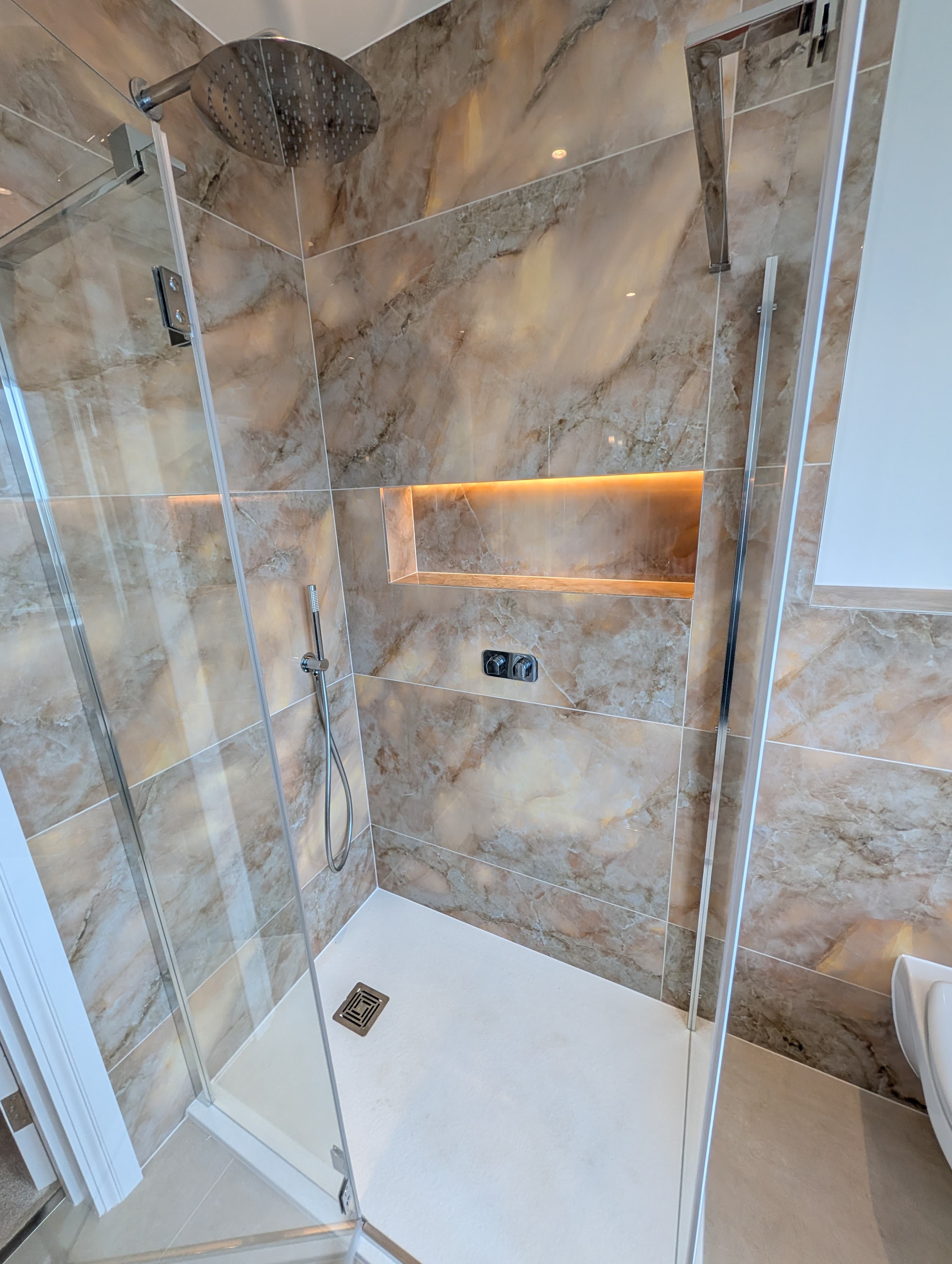 Close-up of a book-matched marble-effect shower wall with a backlit recessed niche and chrome shower controls