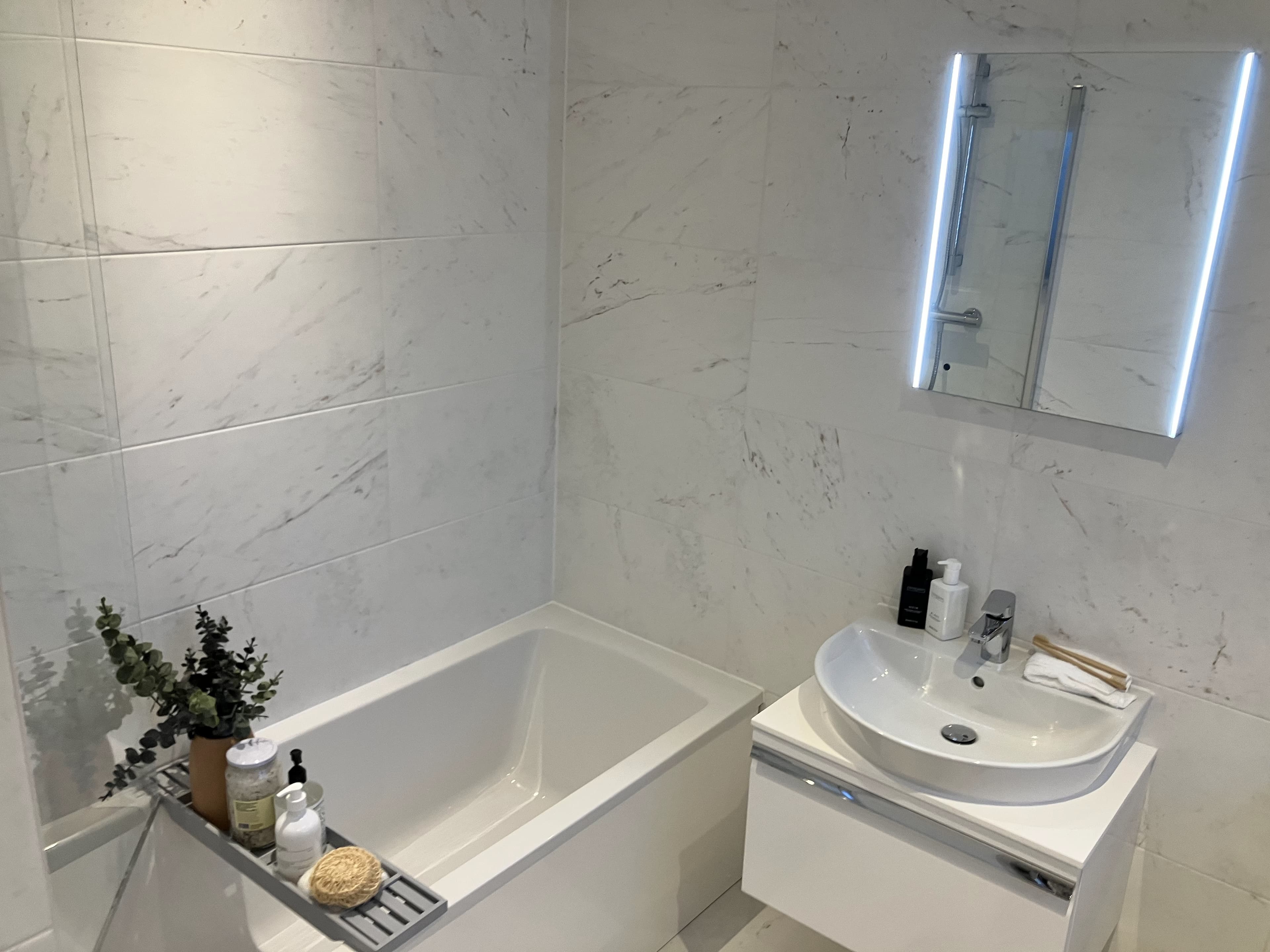 White marble bathroom with bathtub and illuminated mirror