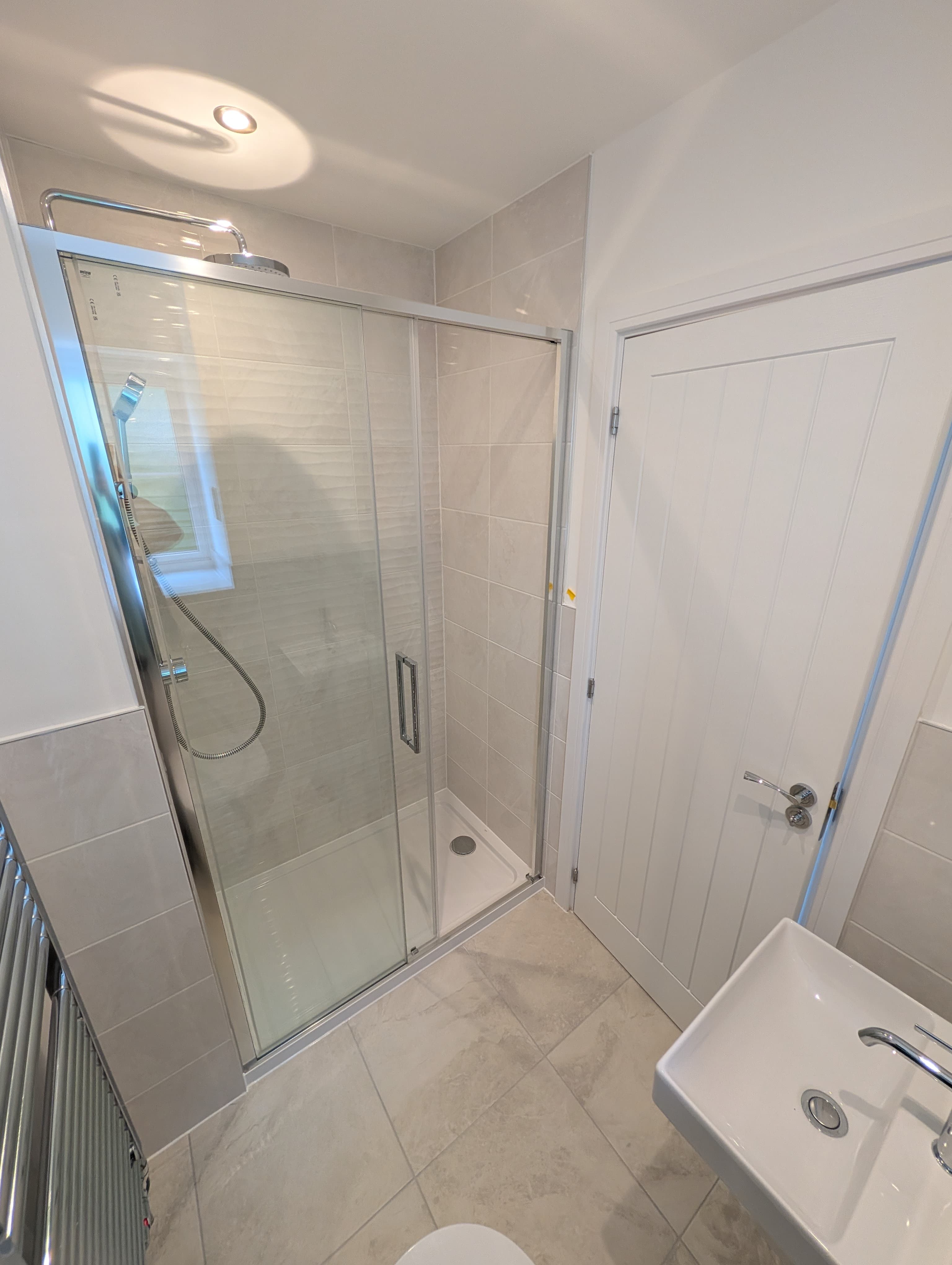 Glass-enclosed shower with sliding door and neutral tiling