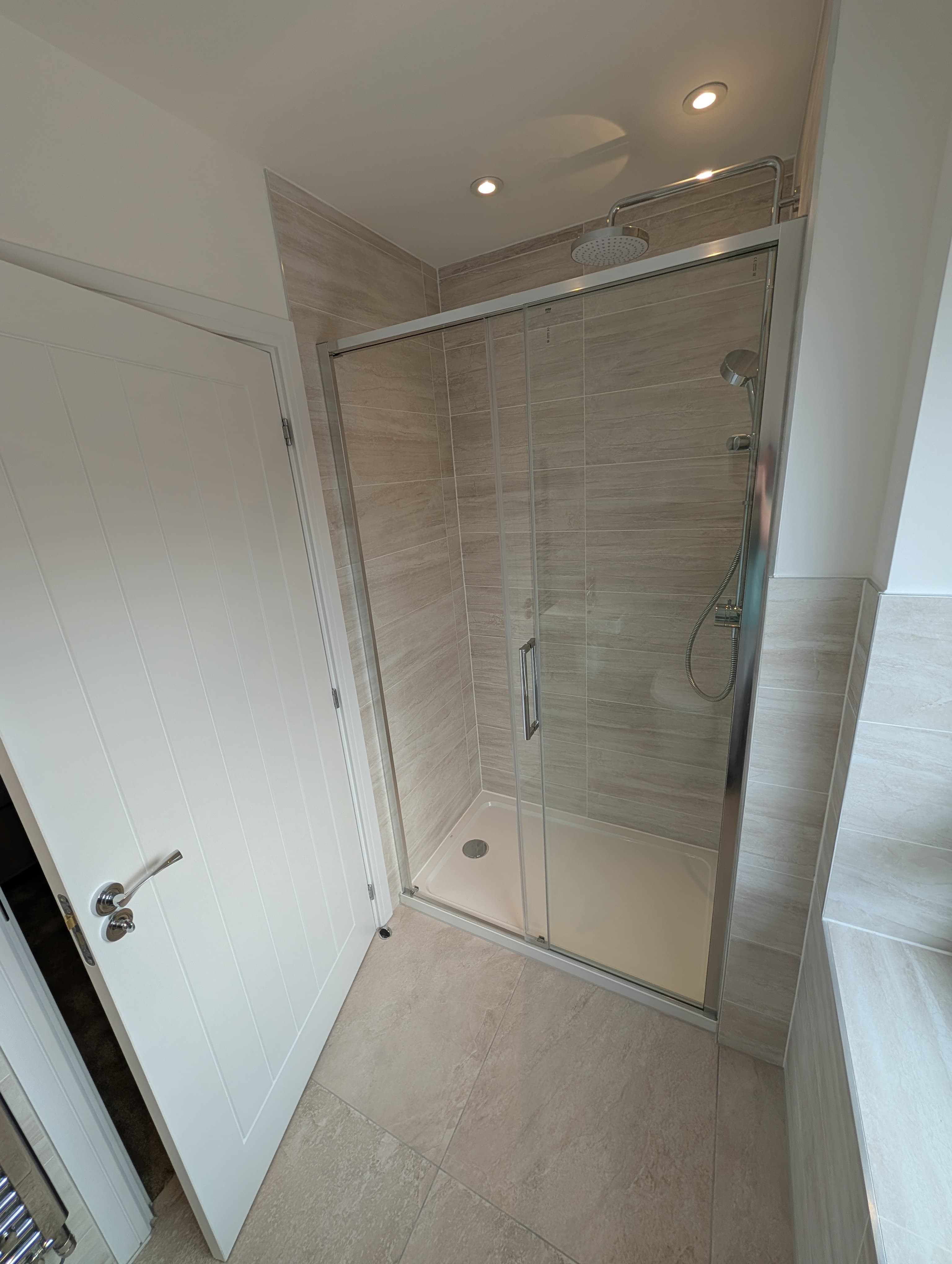 Glass shower enclosure with rainfall shower head and neutral tiling