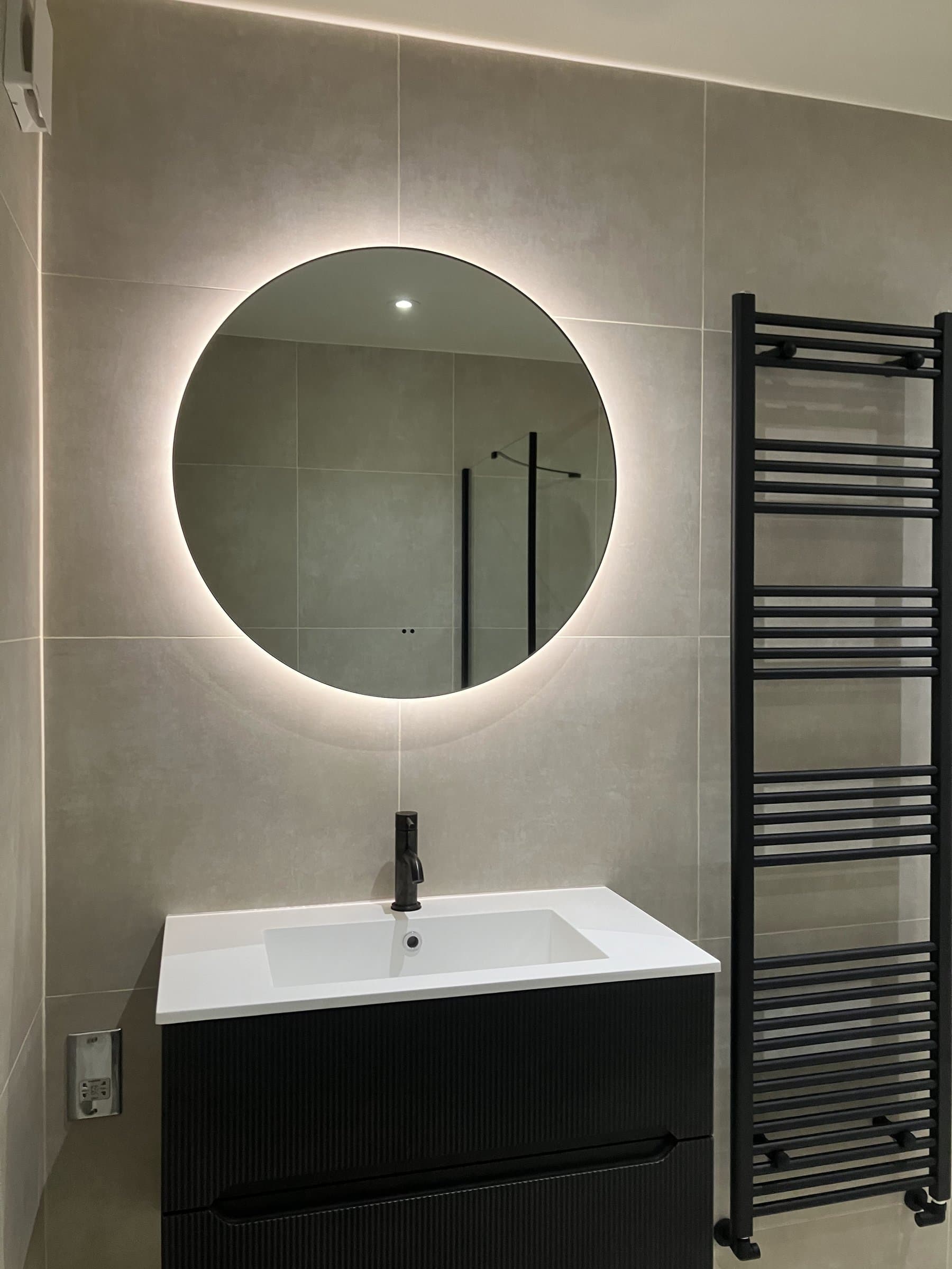 Modern bathroom renovation with illuminated round mirror and black vanity